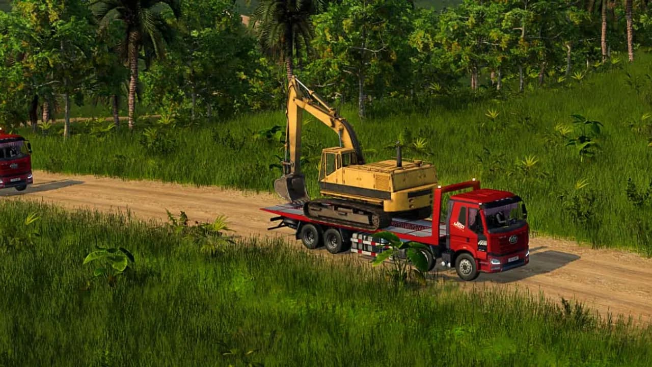 Camião vermelho a transportar uma escavadora por um caminho de terra
